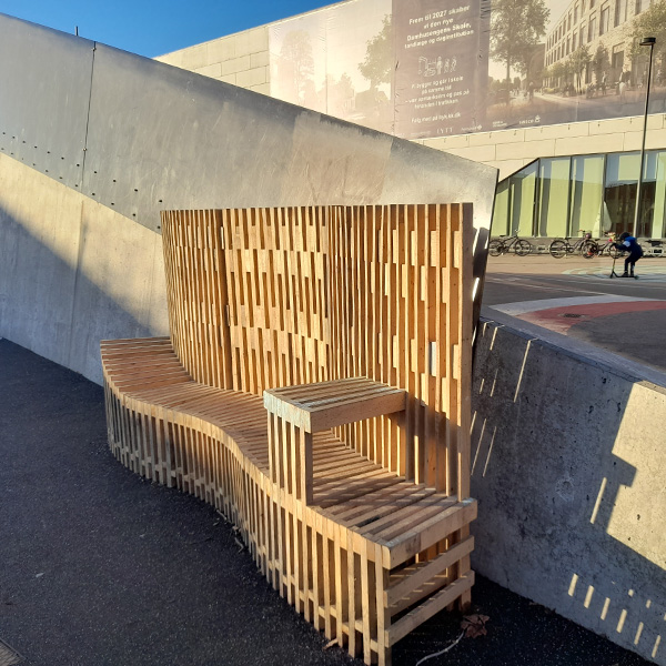 Lamelbænk med ryglæn opsat ved Damhusengens skole i Vanløse. Der er leveret 30 meter bænk med forskellig udformning.